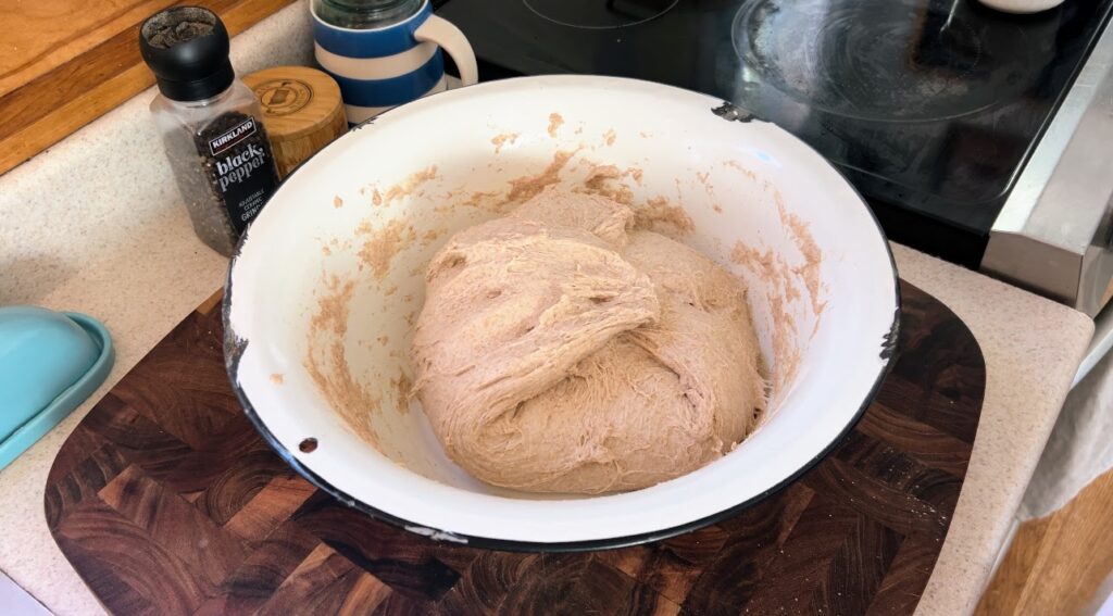 Hearty whole wheat sourdough dough in large white enamelware bowl.