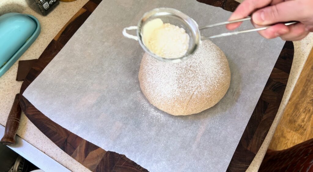 Dusting sourdough dough with flour on parchment paper.