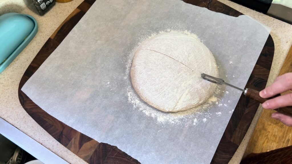 Scoring a loaf of hearty whole wheat sourdough.