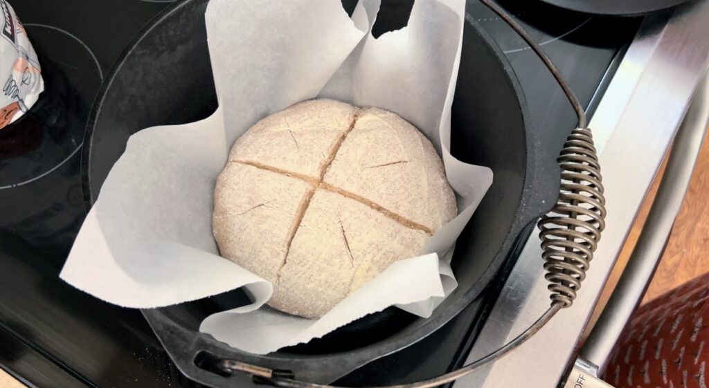 Scored sourdough dough on parchment paper in a black cast iron dutch oven. 