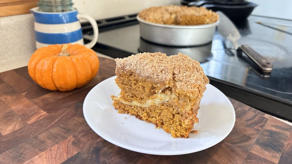 Slice of Pumpkin Cream Cheese Coffee Cake on a white plate next to a mini orange pumpkin.