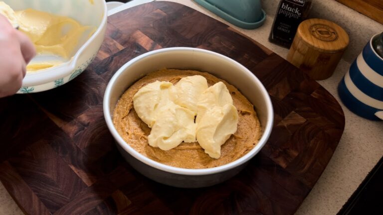 Cream cheese filling being spooned on top of pumpkin coffee cake batter.