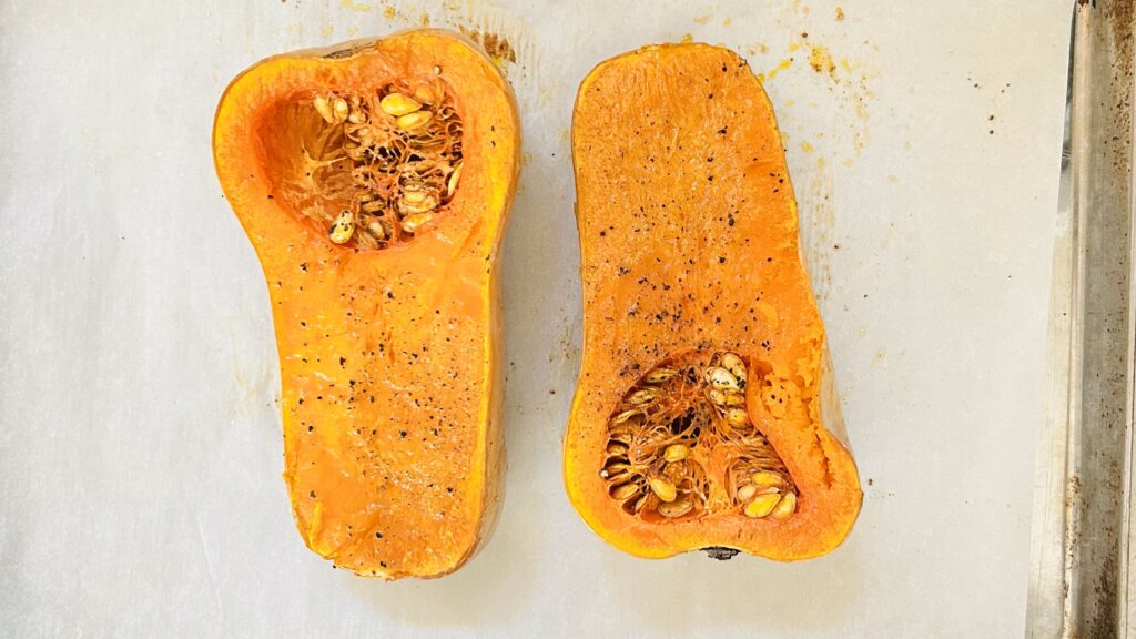 Roasted butternut squash on a parchment paper lined baking sheet seasoned with salt and pepper.