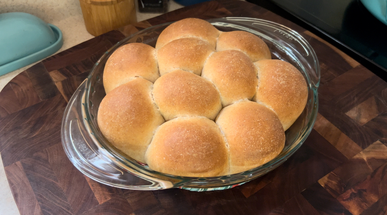 Freshly baked honey wheat dinner rolls in a round pie pan on a wooden cutting board.