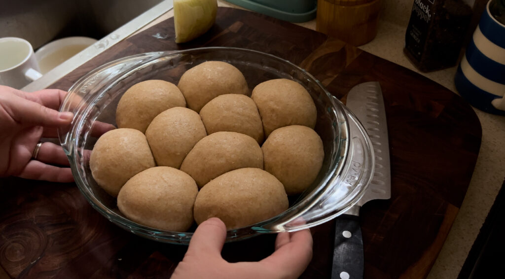 Dough for soft and fluffy honey wheat dinner rolls that has risen in round pie pan and are ready to go into the oven for baking.