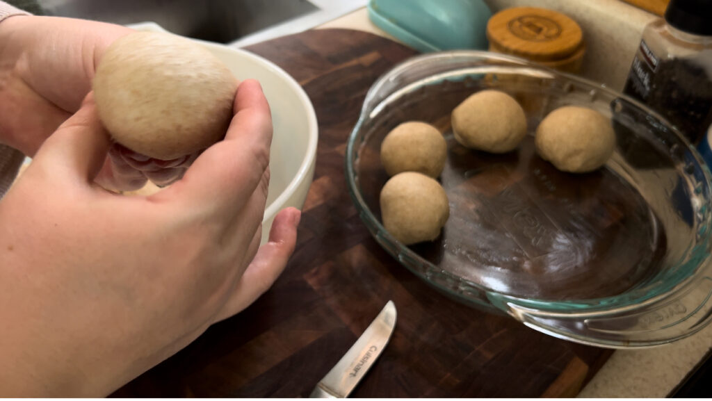 Women shaping dough balls for soft and fluffy honey wheat dinner rolls and placing them in round, glass pie pan.