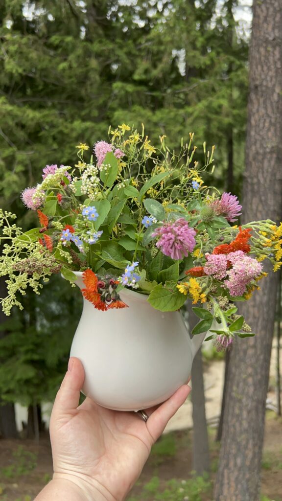 Bouquet of pink, red, yellow, white and orange wildflowers in a white pitcher being held up for the picture