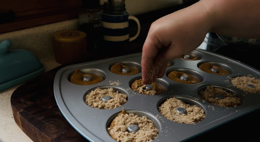 Sprinkling streusel crumb topping on top of pumpkin donut batter before baking.