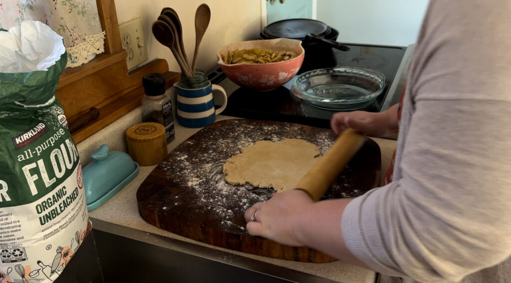 Rolling out pie crust on a wooden cutting board with a rolling pin.