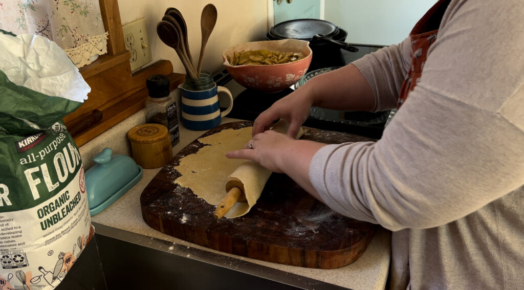 Rolling pie crust dough onto a wooden rolling pin.