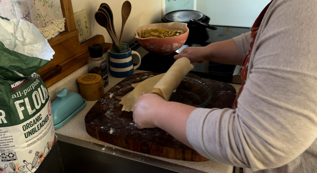 Rolling pie crust dough into a round glass pie dish for baking.