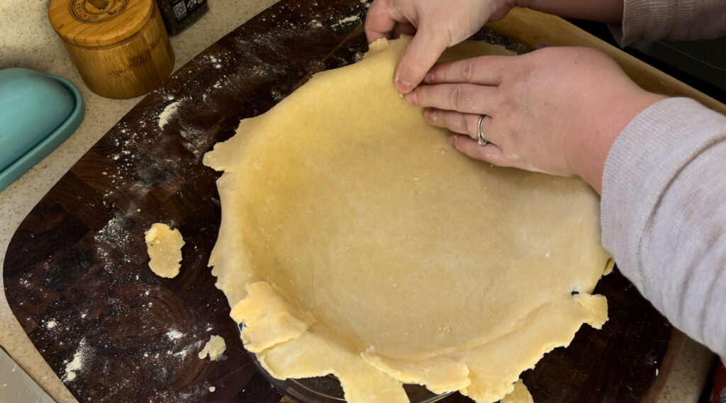 Pressing pie crust dough into a glass pie dish.