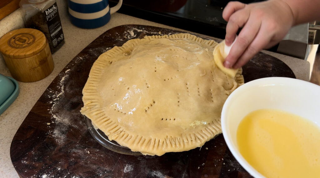 Brushing the top of a pie crust with an egg wash.