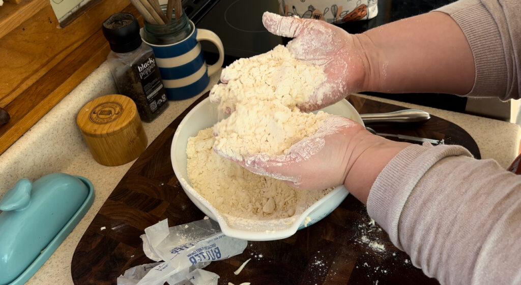 Two hand holding a mixture of butter, flour, sugar and salt for making pie crust.