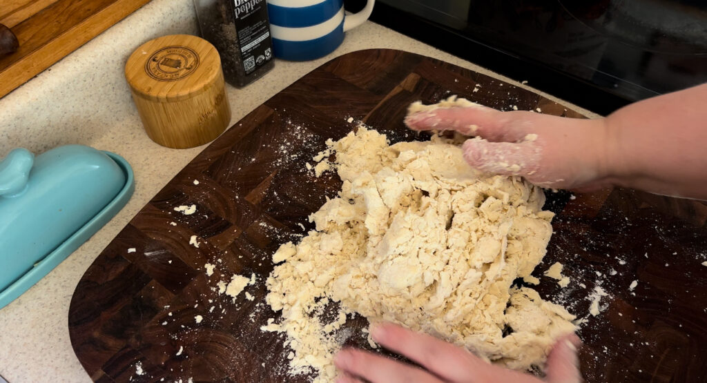 Mixing pie crust dough by hand on a wooden cutting board.