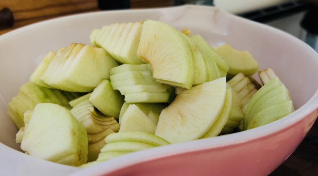 Peeled, cored and chopped granny smith apples in a pink bowl for rustic apple pie.