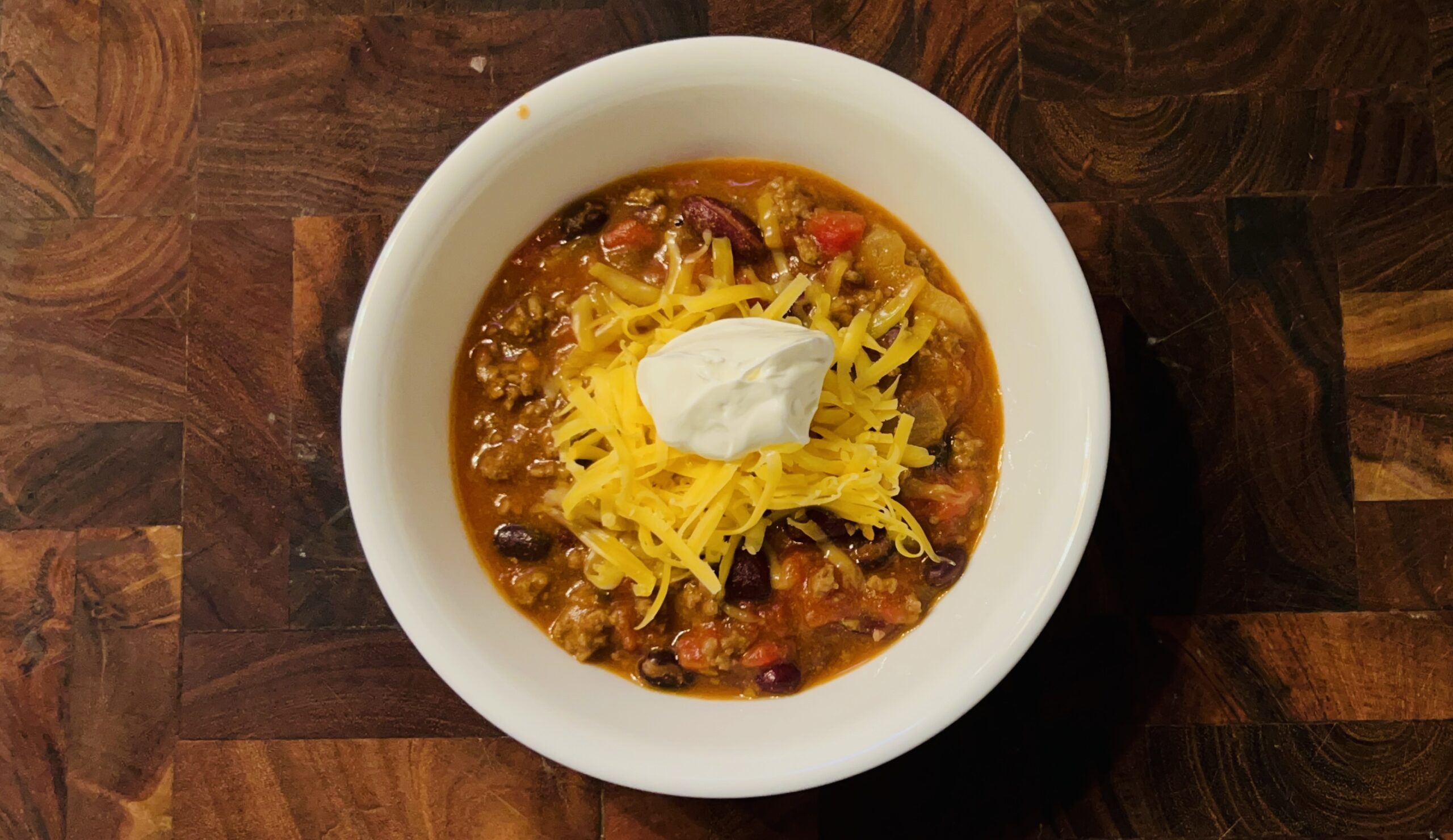 Bowl of easy slow cooker chili topped with shredded cheddar cheese and a dollop of sour cream.