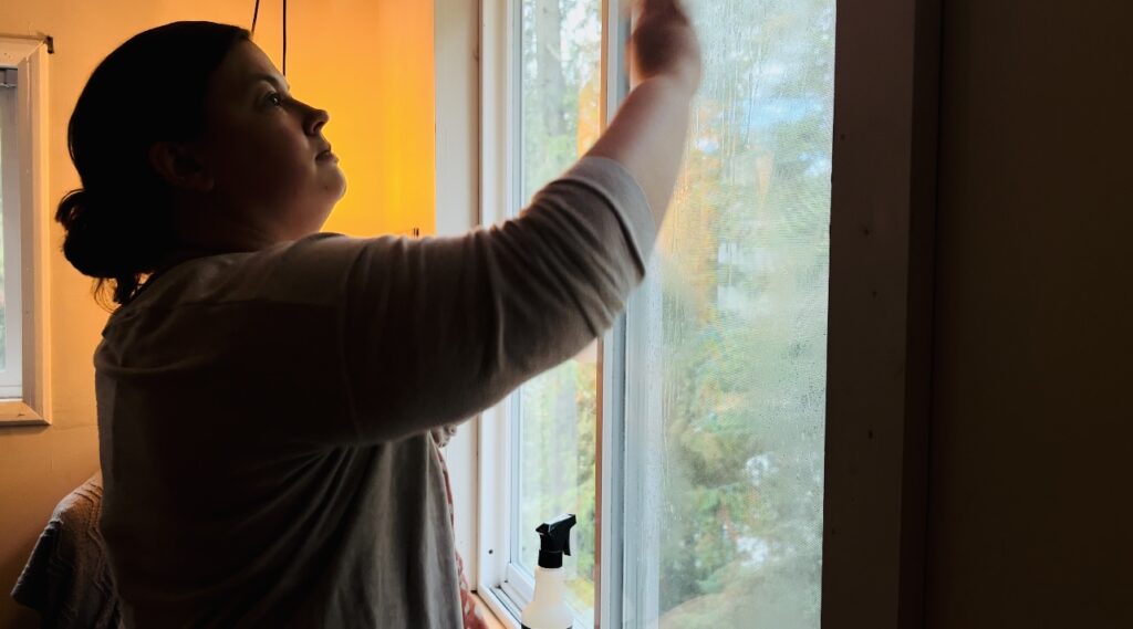 Woman washing her window with golden light shining behind her.