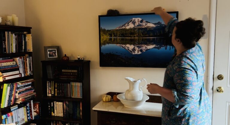 Woman dusting a picture frame with a picture of a mountain.