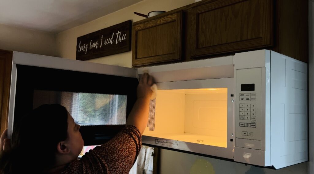 Woman cleaning her microwave that is above her oven.