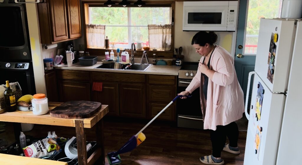 Woman in a pink duster sweater mopping her kitchen floor with a Swiffer Wet Jet mop.