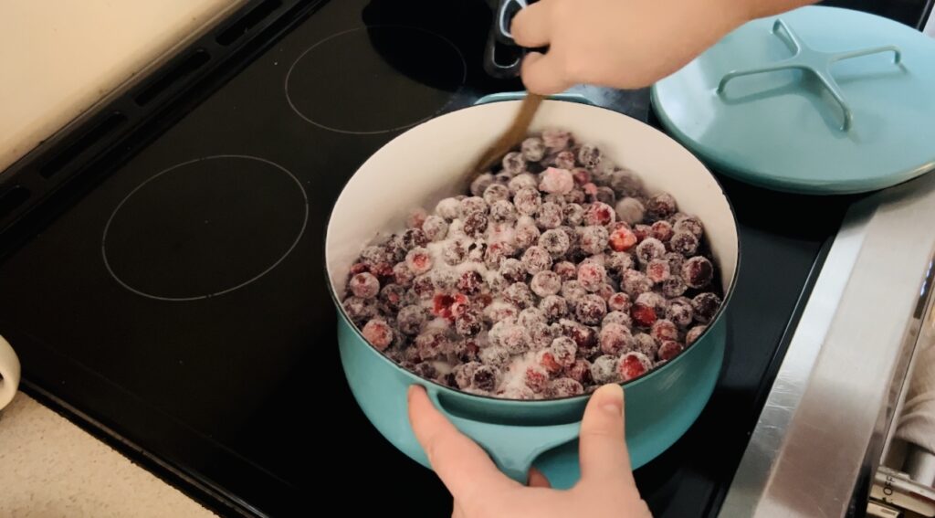 Fresh cranberries in a turquoise sauce pan with sugar slowly cooking for easy homemade cranberry sauce.