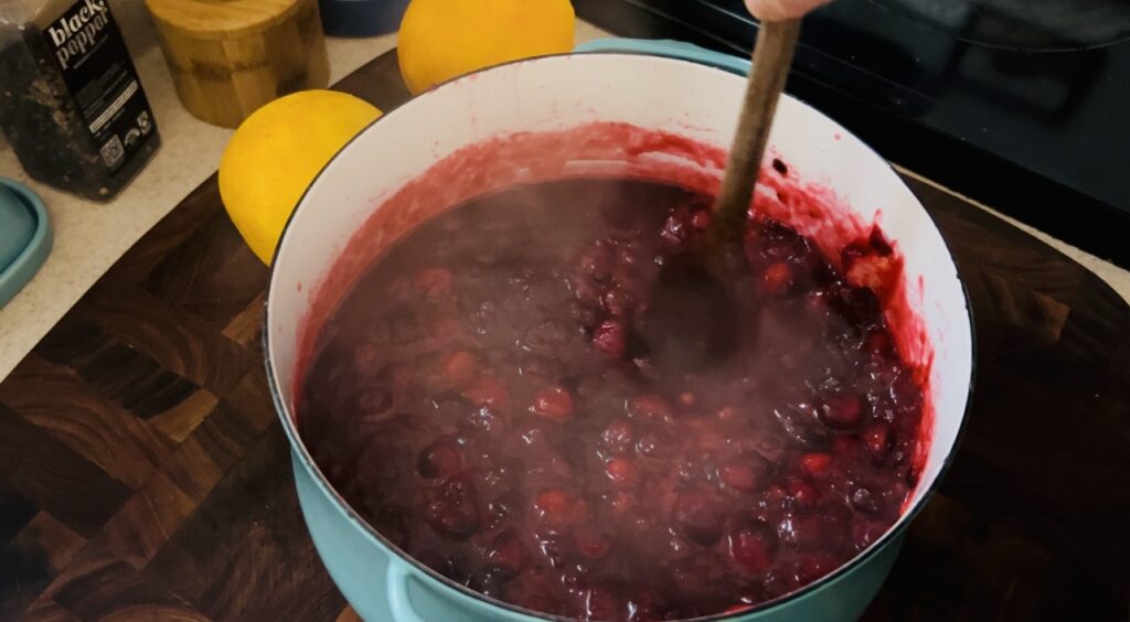 Cooking cranberries in a turquoise sauce pan being stirred with a wooden spoon.