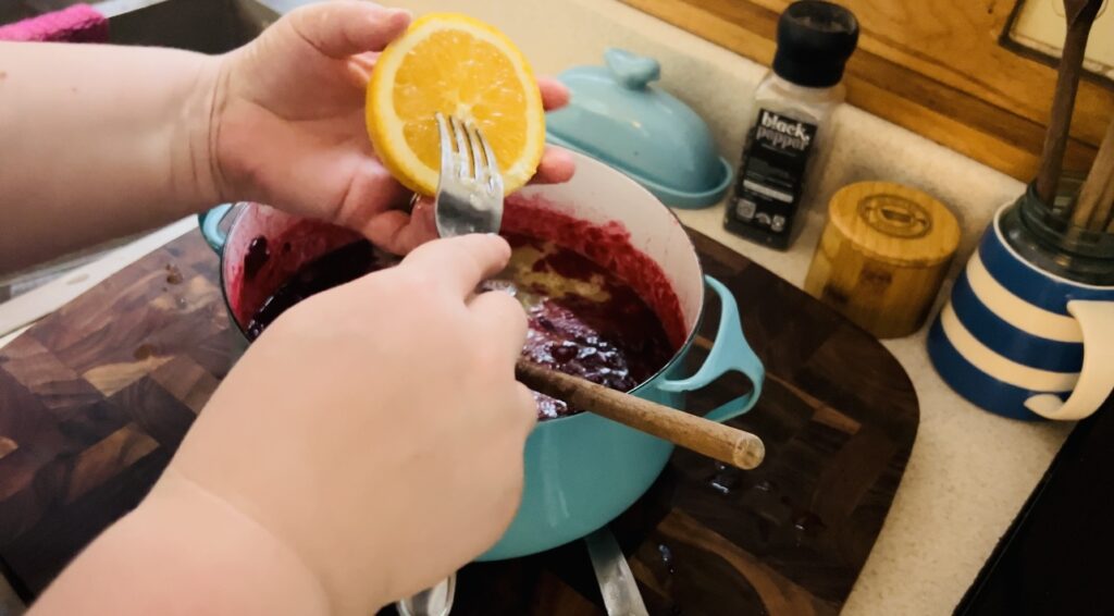 Juicing an orange with a fork into cooked cranberries for easy homemade cranberry sauce.