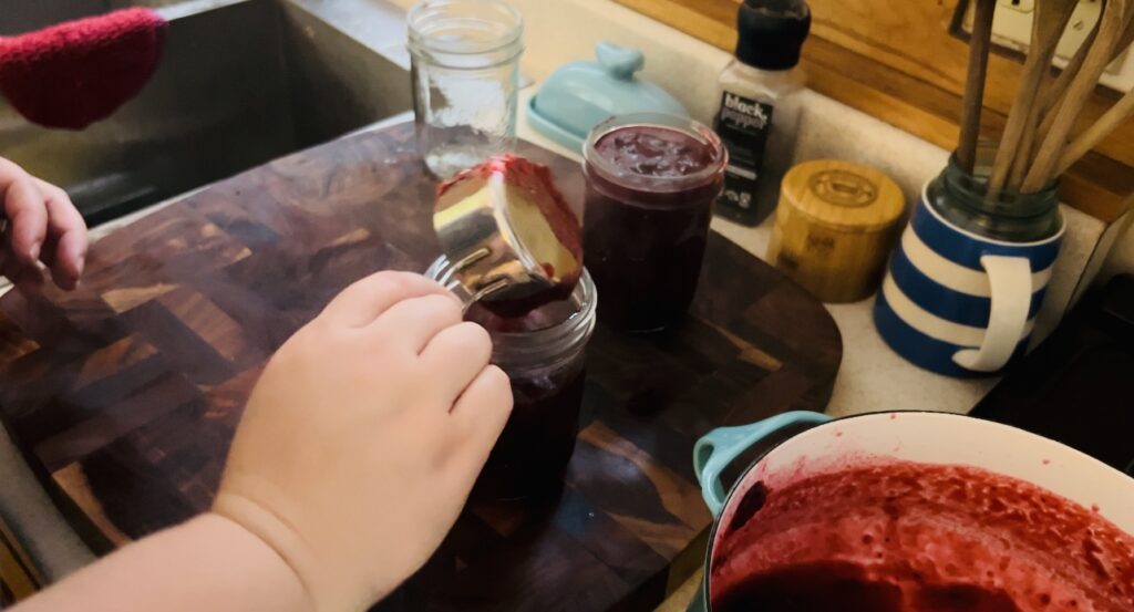 Scooping cooked cranberry sauce into mason jars for storing.