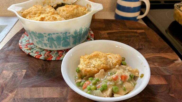 Bowl of leftover turkey casserole with peas and carrots in a vintage Pyrex casserole dish with turquoise farm scene.