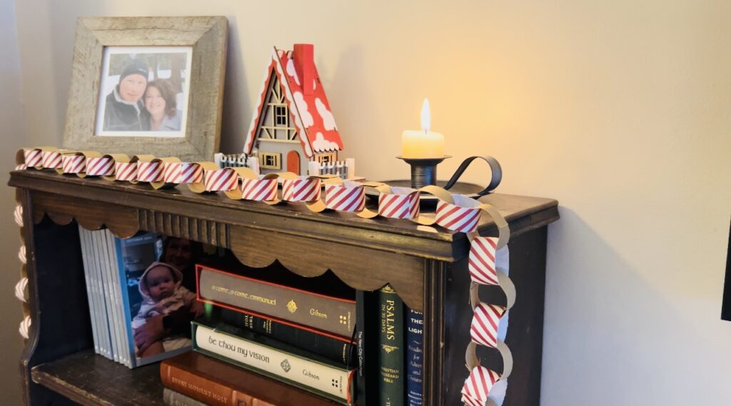 Christmas paper chain garland strung over an old bookshelf with a wooden Christmas house and candle burning. 