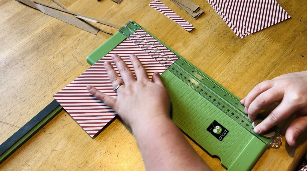 Cutting strips of red striped paper for a Christmas paper chain garland.