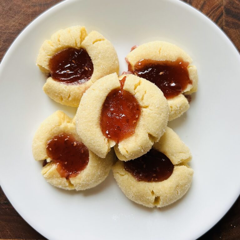 White plate with five freshly baked raspberry thumbprint cookies.