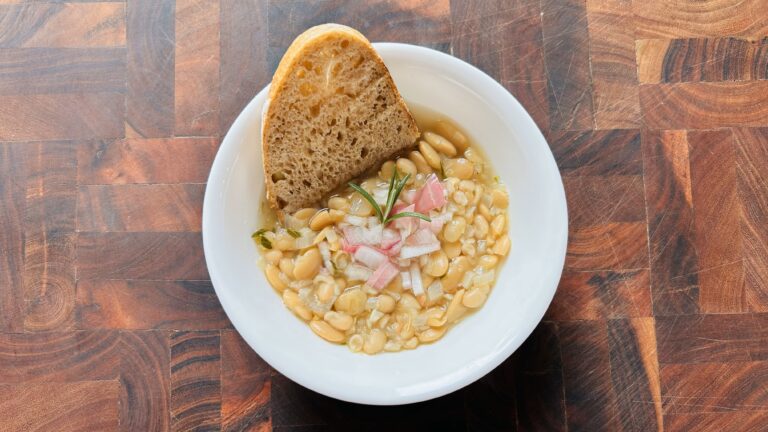 Bowl of white bean and shallot soup with rosemary and garlic with a slice of whole wheat sourdough bread.