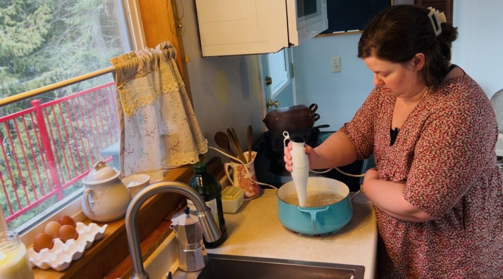 Woman using an immersion blender to blend up some soup.