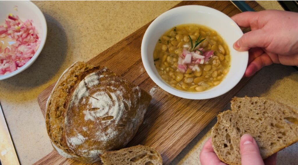 Bowl of white bean and shallot soup with rosemary and garlic topped with some quick pickled shallots and served with whole wheat sourdough bread.