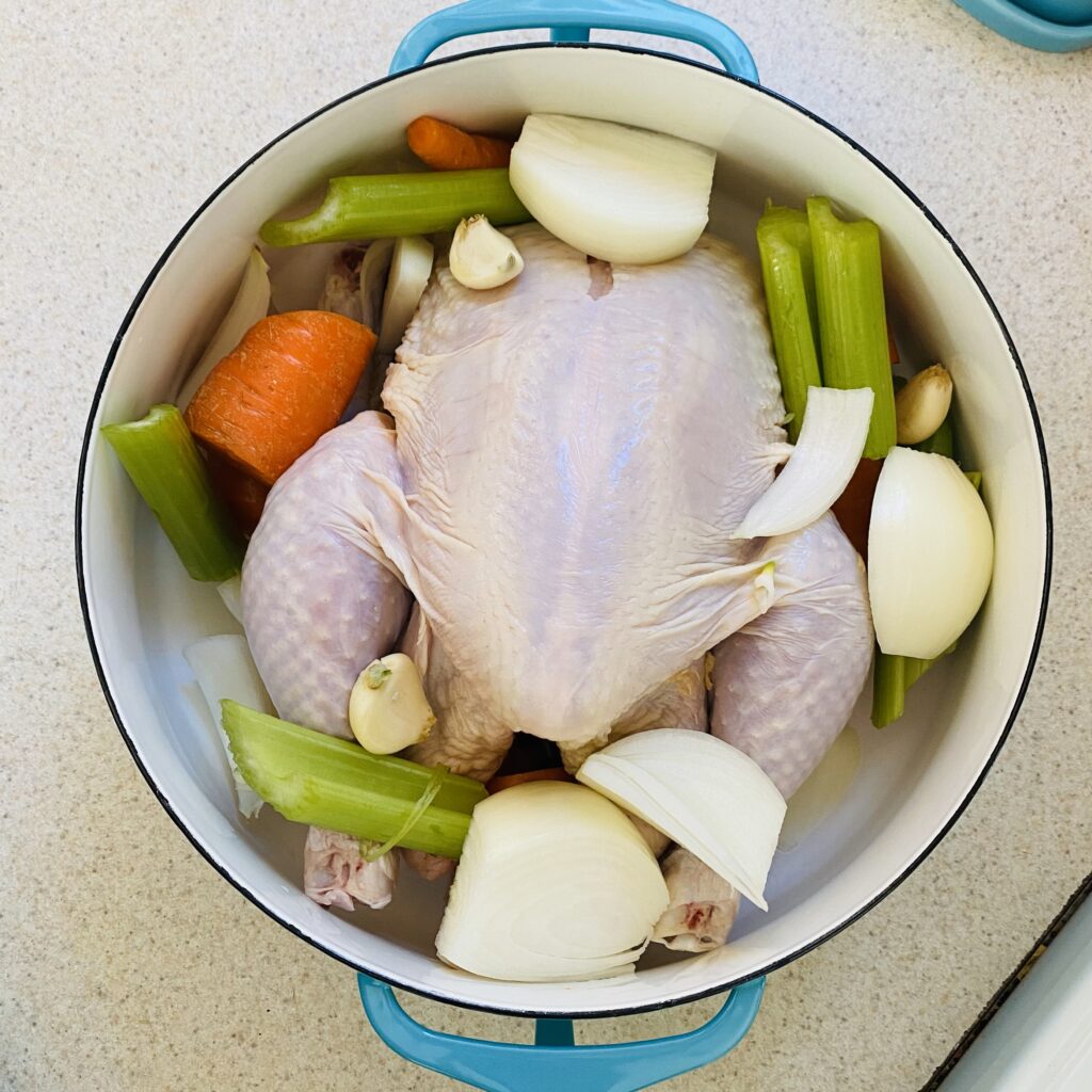 Whole chicken in a pot with celery. carrots, onions and garlic for making chicken broth.