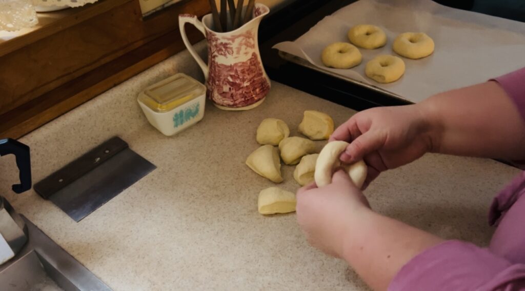 Woman shaping sourdough bagel dough into the bagel shape and placing on a parchment paper lined cookie sheet.