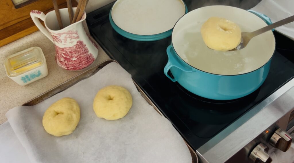 Placing boiled sourdough bagel dough onto a parchment lined cookie sheet. 