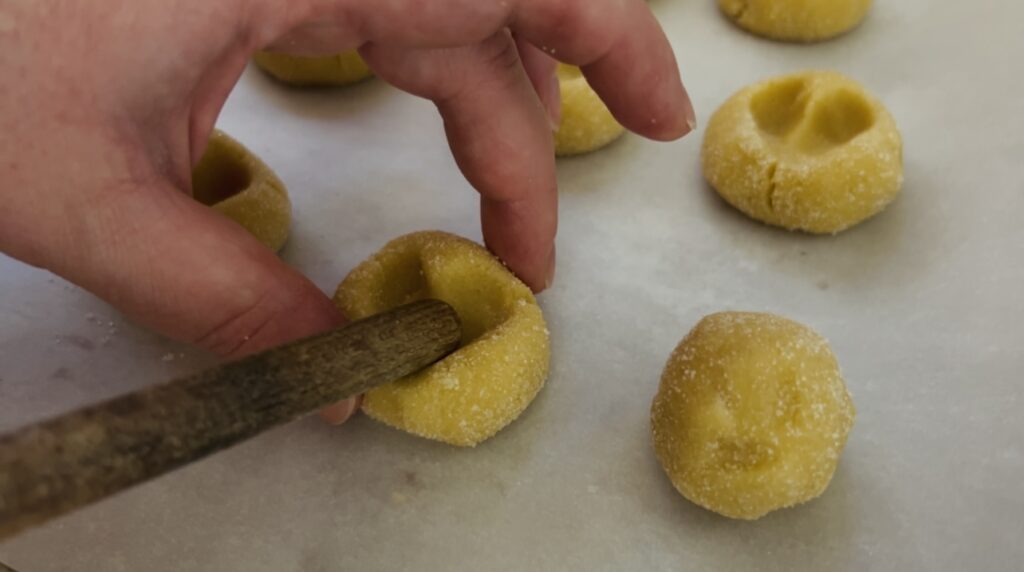 Pressing the heart shape into strawberry thumbprint cookies.