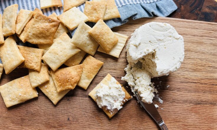 Wood cutting board with freshly baked easy sourdough discard crackers and an herbed soft cheese spread.