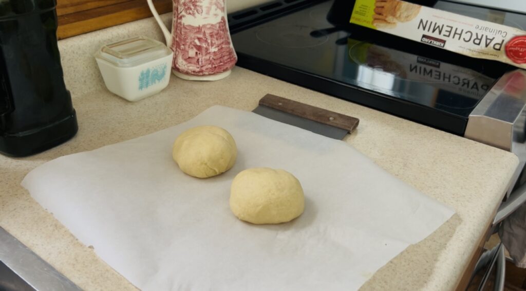 Two balls of cracker dough resting on parchment paper before being rolled out.