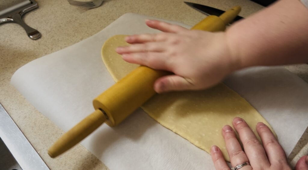 Rolling out sourdough cracker dough with a rolling pin on parchment paper.