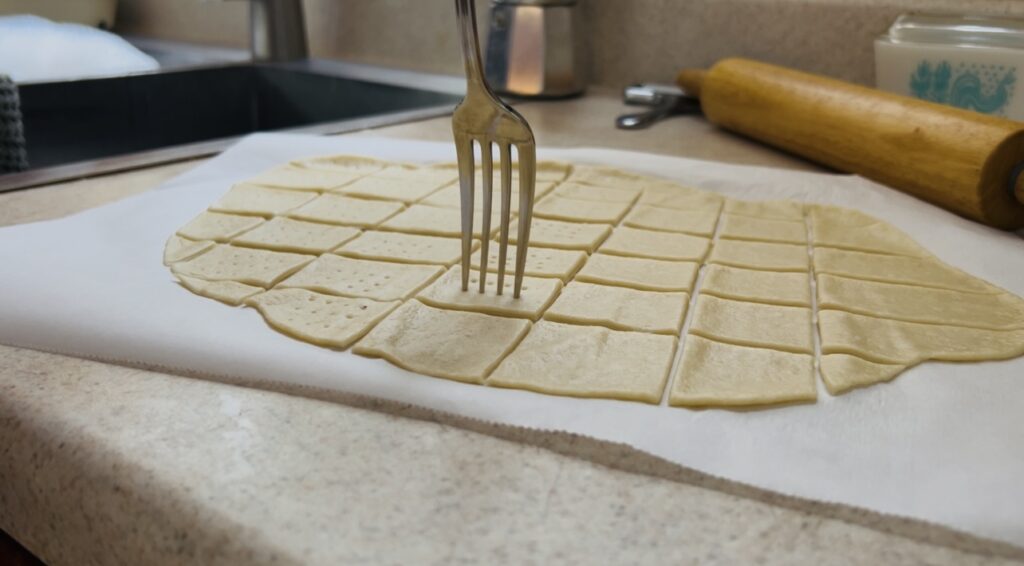 Pricking sourdough cracker dough with a fork before baking.