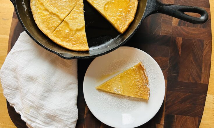 Slice of a sourdough dutch baby pancake next to a cast iron skillet with the rest of the dutch baby.