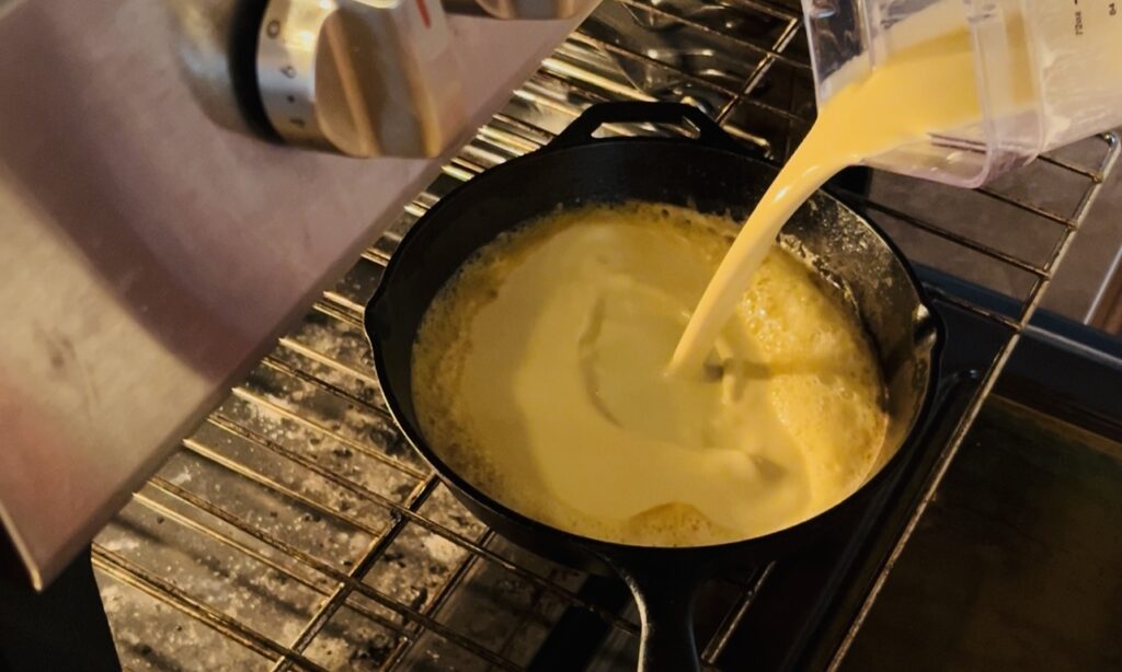 Pouring Dutch baby batter into a preheated hot cast iron skillet.