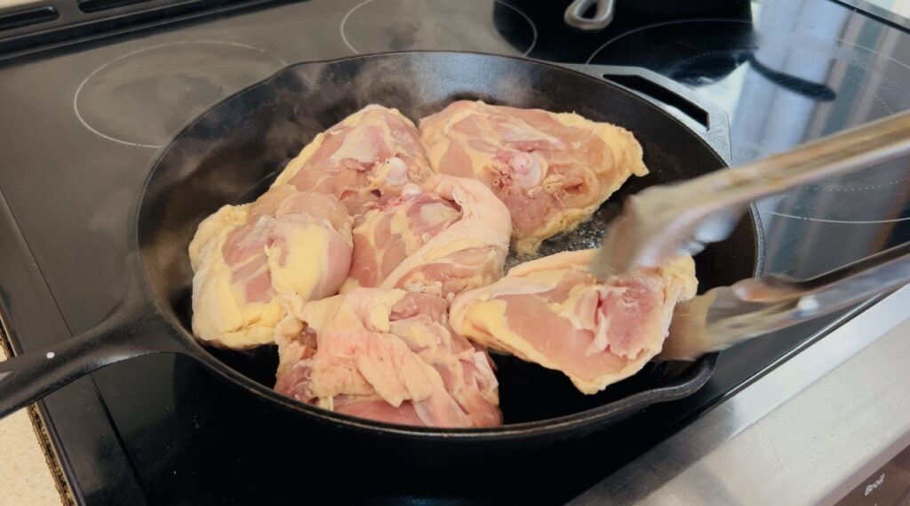 Chicken thighs cooking in a cast iron skillet.