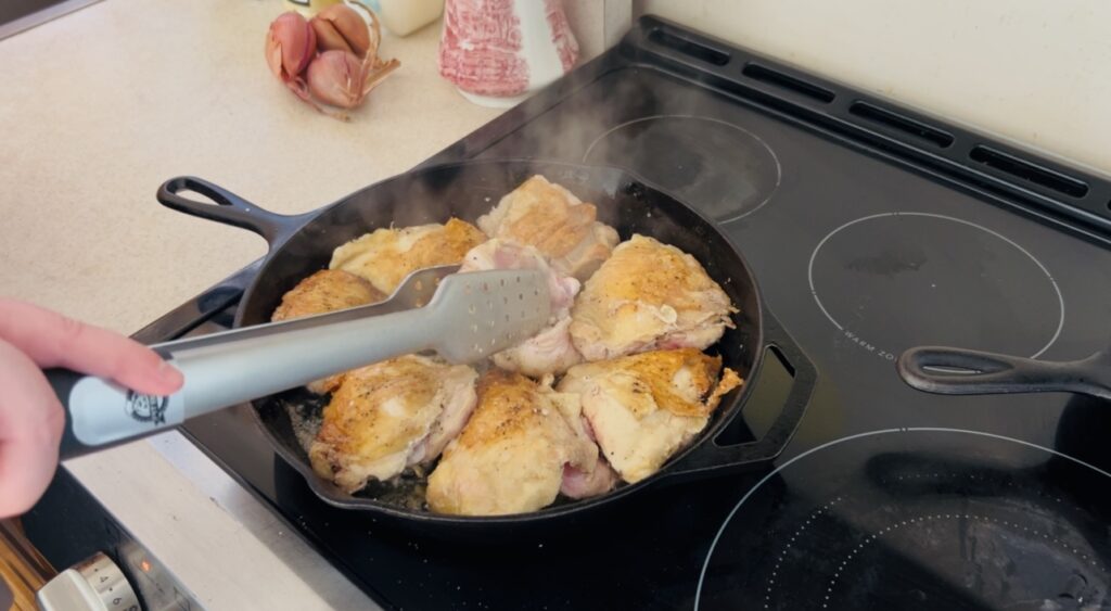 Chicken thighs cooking in a large cast iron skillet.