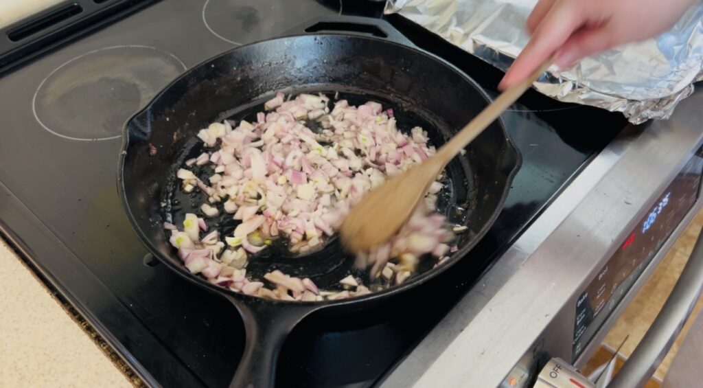 Shallots sauteing in a large cast iron skillet.