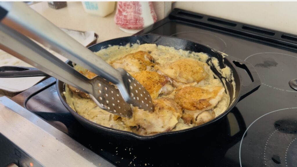 Chicken thighs in a shallot, mushroom and mustard cream sauce in a large cast iron skillet.